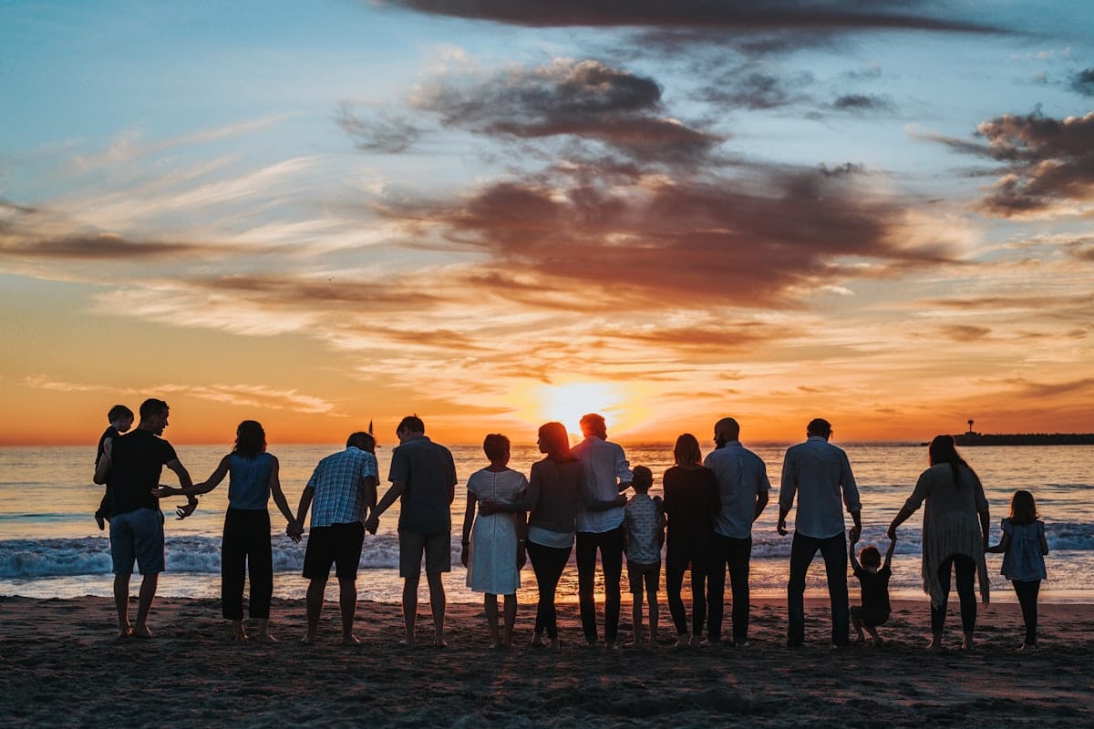 An extended family standing together on a beach at sunset.